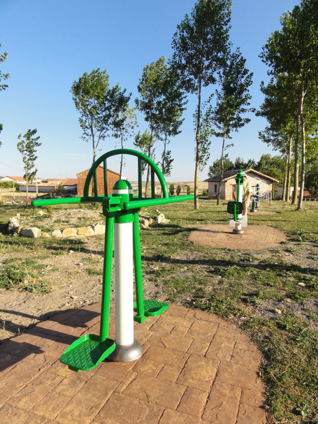 Eine grüne und weiße Spielplatzstruktur steht in einem Park, umgeben von Bäumen, Häusern und einem klaren blauen Himmel, mit saftig grünem Gras, das den Boden bedeckt.