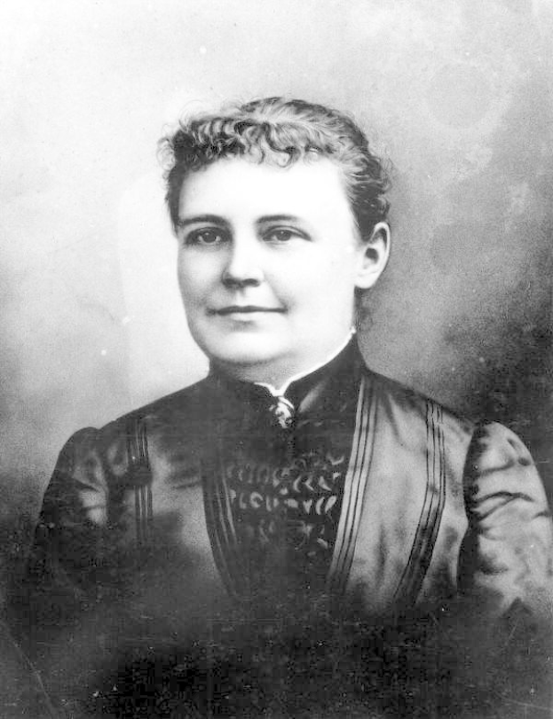 Schwarzes und weißes Foto einer Frau in einem Kleid, die mit verschränkten Händen und erhobenem Haupt steht und Entschlossenheit und Stärke ausstrahlt.