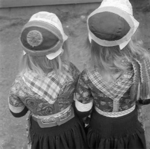 Zwei junge Mädchen in traditionellen bayrischen Kleidern und Hüten stehen nebeneinander vor einer Wand, dargestellt in Schwarz-Weiß.