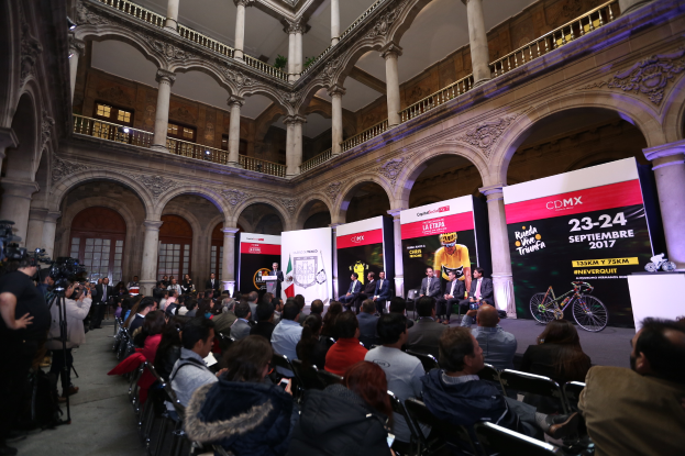 Eine Gruppe von Menschen, die an einem Tisch mit einem Rednerpult und einem Mikrofon vor einer Menge, Kameras und Bannern sitzen, während einer Pressekonferenz für das CDMX 2017-Event.