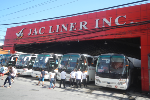 Eine Gruppe von Bussen vor einem Gebäude mit einer "Jac Liner Inc." -Plakette geparkt, mit Menschen im Vordergrund und Drähten und einem klaren blauen Himmel im Hintergrund.