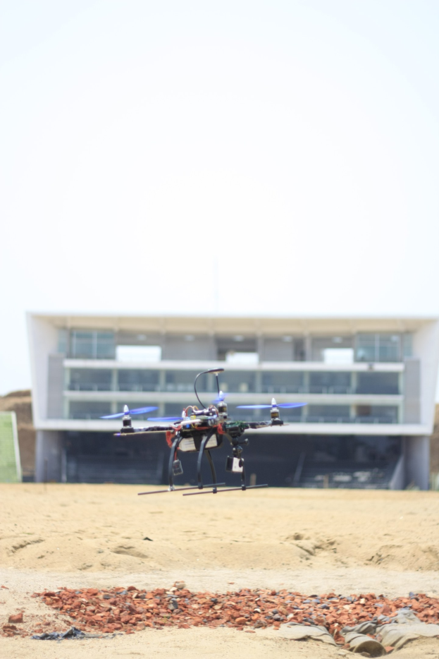 Ein kleiner Drohne fliegt über einen sandigen Strand neben einem Gebäude, mit dem Himmel im Hintergrund.