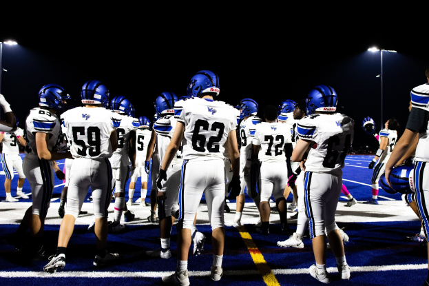 Eine Gruppe von Fussballspielern in Helmen und Stiefeln steht auf einem Feld unter hellen Stadionlampen und sieht bereit für ein Spiel aus.