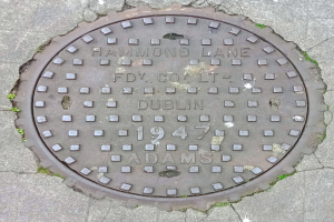 Ein metallener Gullideckel auf einer Straße in Dublin, Irland, mit eingravierten Text.