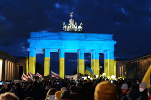 Eine Menschenmenge steht vor dem Brandenburger Tor in Berlin, Deutschland, mit Fahnen und Plakaten, auf denen ein Banner auf der rechten Seite des Bildes zu sehen ist.