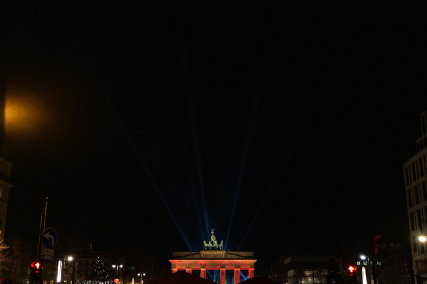 Brandenburger Tor bei Nacht, beleuchtet von Straßenlaternen, umgeben von Gebäuden, Bäumen, Pfählen, Verkehrsampeln, Schildern und Zelten unter einem dunklen Himmel.
