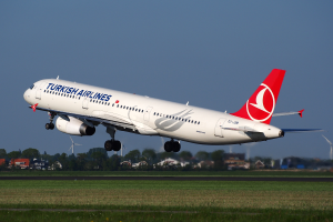 Ein Airbus A330-300 der Turkish Airlines startet vom Frankfurter Flughafen, mit Gras, Gebäuden, Bäumen und Windmühlen im Hintergrund unter einem klaren blauen Himmel.