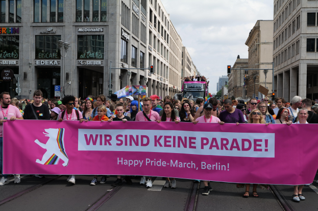 Eine Gruppe von Menschen geht auf einer Straße in Berlin, Deutschland, mit einem pinken Banner mit der Aufschrift "Happy Pride March"