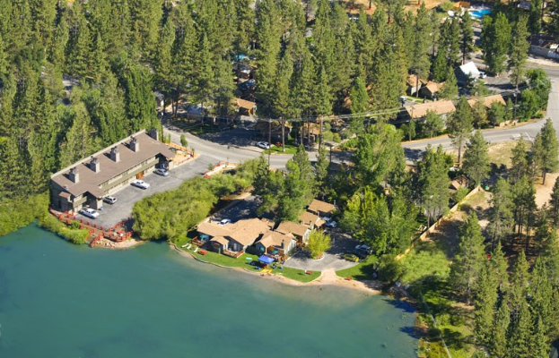 Luftbild eines Resorts am Seeufer, umgeben von Bäumen, Häusern, Fahrzeugen, Straßen, Masten und Gras, mit dem See unten sichtbar.