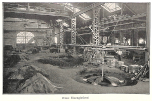 Schwarzes und weißes Foto eines Fabrikinneren mit Arbeitern, die Maschinen bedienen, Metallstangen und -st"utzen, beschriftet mit "Neue Eisenglebeerei, die erste Fabrik in Deutschland" unten.