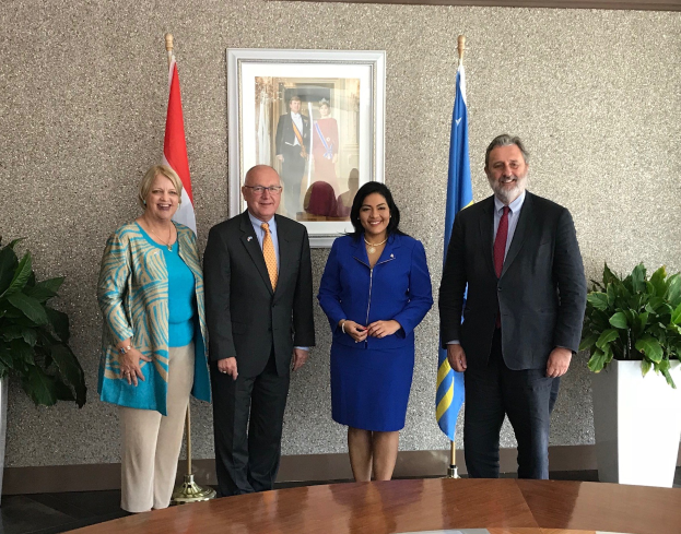 Eine Gruppe von Menschen, die um einen Tisch mit Papieren stehen und lächeln, umgeben von Fahnen, Topfpflanzen und einem gerahmten Foto an der Wand, was das Unterzeichnen eines U.S.-Canada Memorandum of Understanding anzeigt.