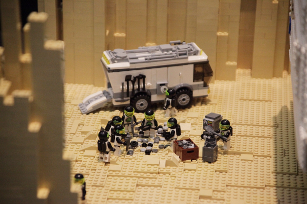 Lego-Modell einer Star-Wars-Szene mit einem Landfahrzeug im Vordergrund und einer Wand im Hintergrund sowie einigen verstreuten Spielzeugen.