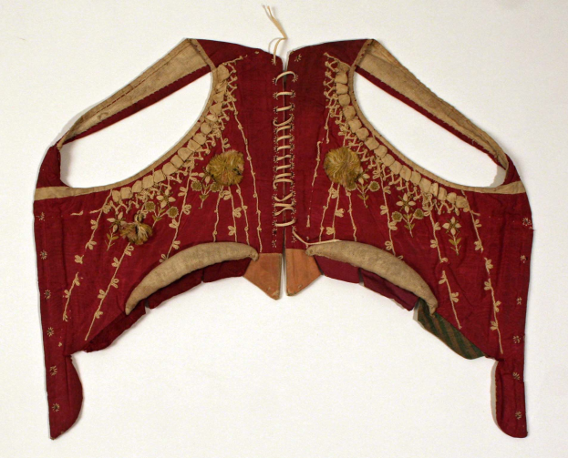 Ein rotes Oberteil mit goldener Stickerei und detaillierten Designs auf einer weißen Oberfläche.