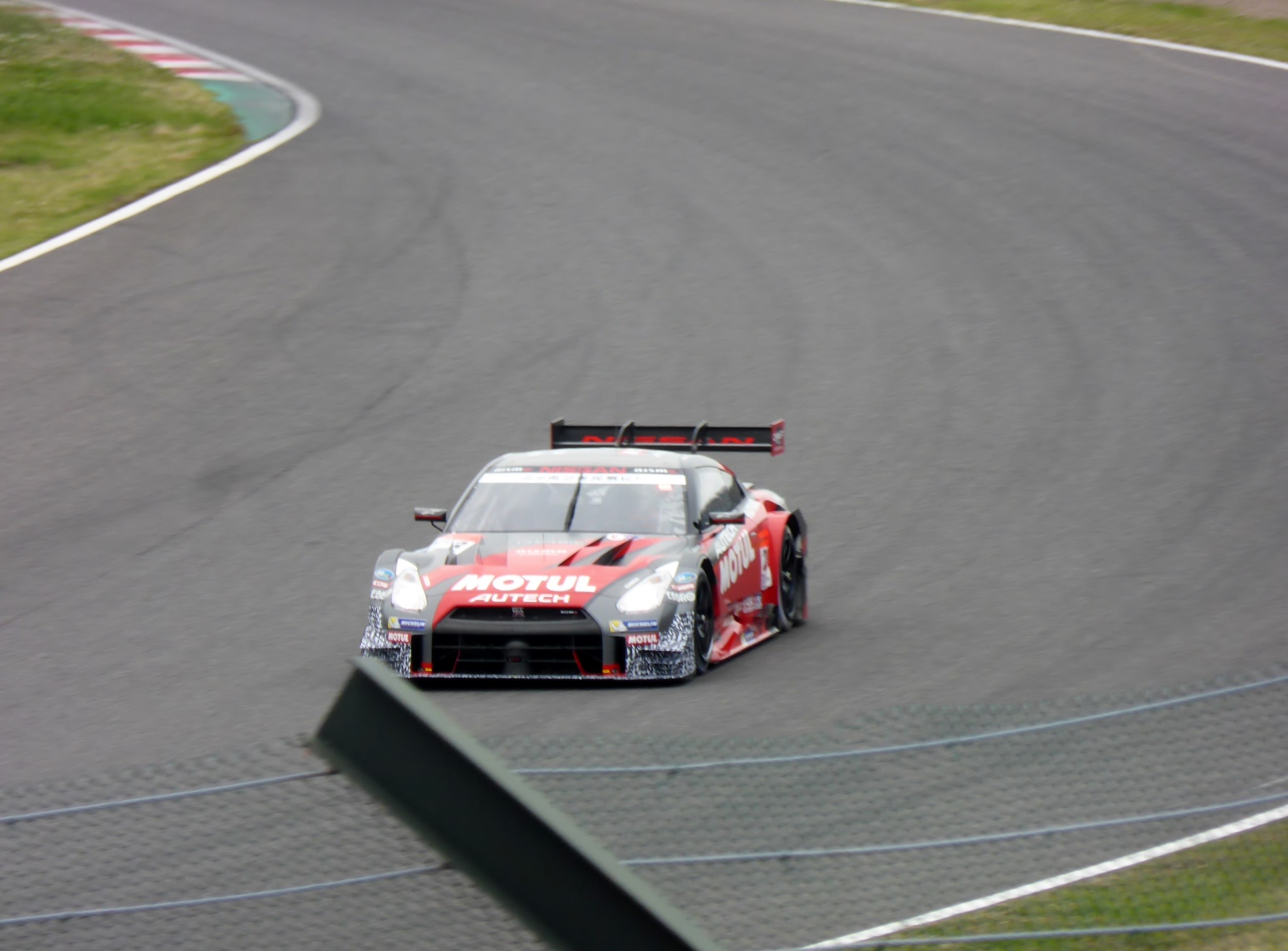 Nissan GT-R Nismo GT3 Rennauto auf der Nürburgring 24 Stunden Strecke, umgeben von grünem Gras auf beiden Seiten.