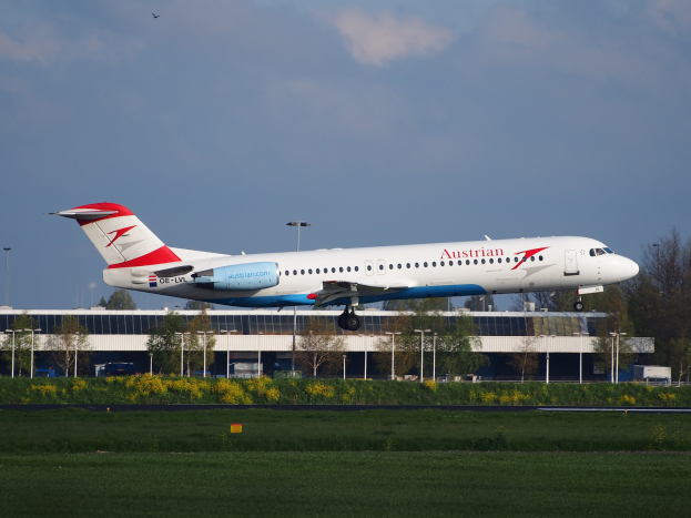 Austrian Airlines Airbus A320-200 beim Starten vom Frankfurter Flughafen mit Grünflächen und einem Gebäude im Hintergrund unter einer bewölkten Himmel.