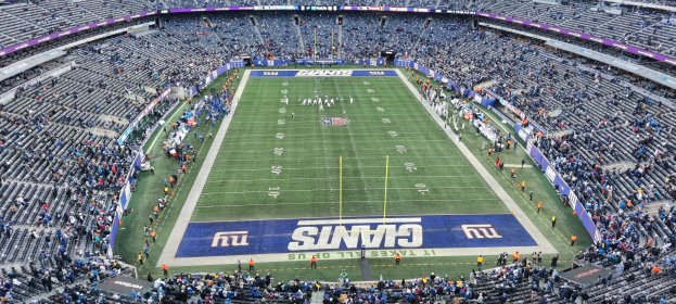 Ein Fußballstadion voller Zuschauer, Spieler, Pfosten und Schilder mit Text, alle in Reihen von Stühlen sitzend.