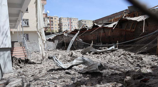 Die Nachwirkungen eines israelischen Luftangriffs in Gaza-Stadt zeigen den Schutt eines eingestürzten Gebäudes auf einer Straße, mit sichtbaren Metallstangen, einem Zaun, einer Treppe, nahegelegenen Gebäuden, Bäumen und einem bewölkten Himmel.