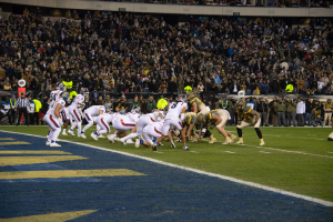 Ein Fußballspiel im Gange mit Spielern in Sportbekleidung und Helmen auf dem Feld, betrachtet von einem Stadionbereich.