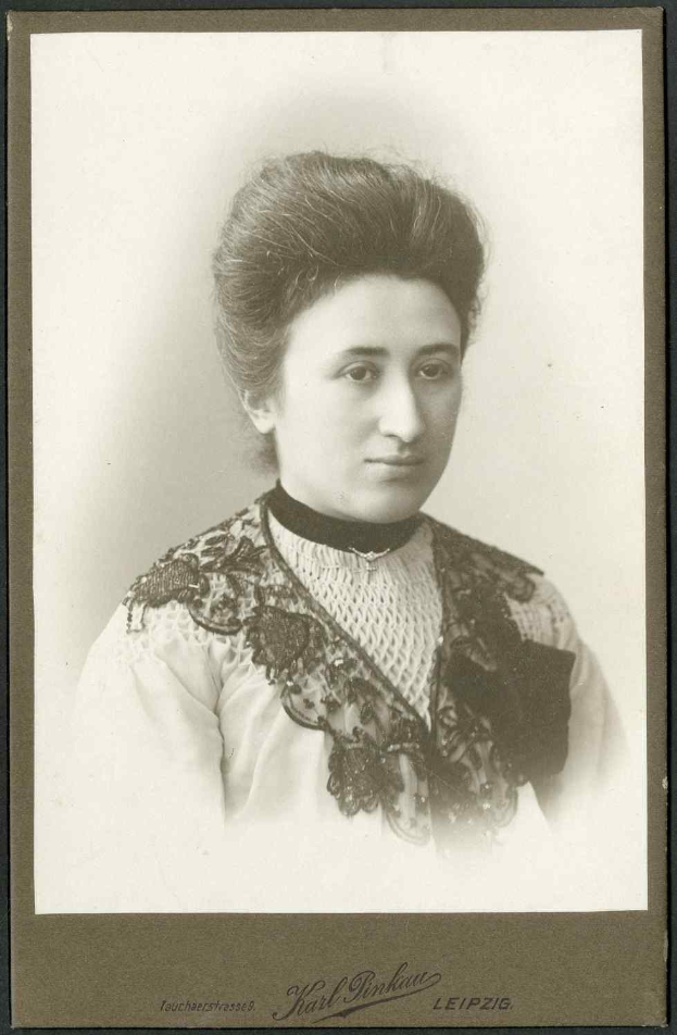 Schwarzes und weißes Porträt einer Frau in einem weißen Kleid mit einem gemusterten Schultertuch, identifiziert als Karl Pinkau Leipzig, die direkt in die Kamera schaut.