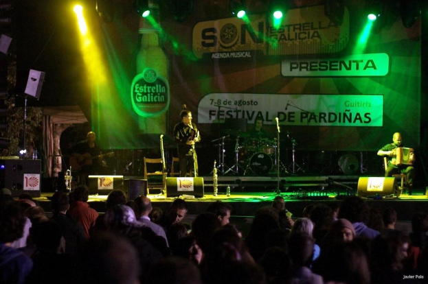 Publikum schaut auf der Bühne mit Musikinstrumenten, Lautsprechern, Mikrofonen, einer Wand, Scheinwerfern und entfernten Gegenständen, einschließlich einer Flasche.