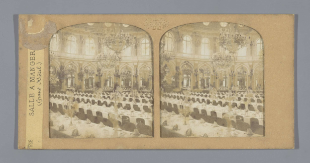 Ein altes Foto eines prächtigen Hotel-Speisesaals mit Tischen, Stühlen, Kronleuchtern und Fenstern, das ein Schild mit der Aufschrift "Sale à Manger, Grand Hotel" links zeigt.