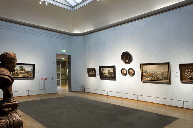 Ein prächtiger Museumsraum mit einer Statue links, Teppichboden, Fotorahmen an den Wänden, einer Glasdecke mit Lichtern und Türen im Hintergrund.