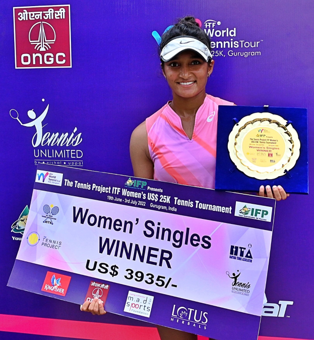 Eine Frau auf einem Tennisplatz, die eine Trophäe und eine Tafel mit der Aufschrift "Frauen-Einzel-Siegerin" hält und eine Mütze trägt, vor einem Banner im Hintergrund.