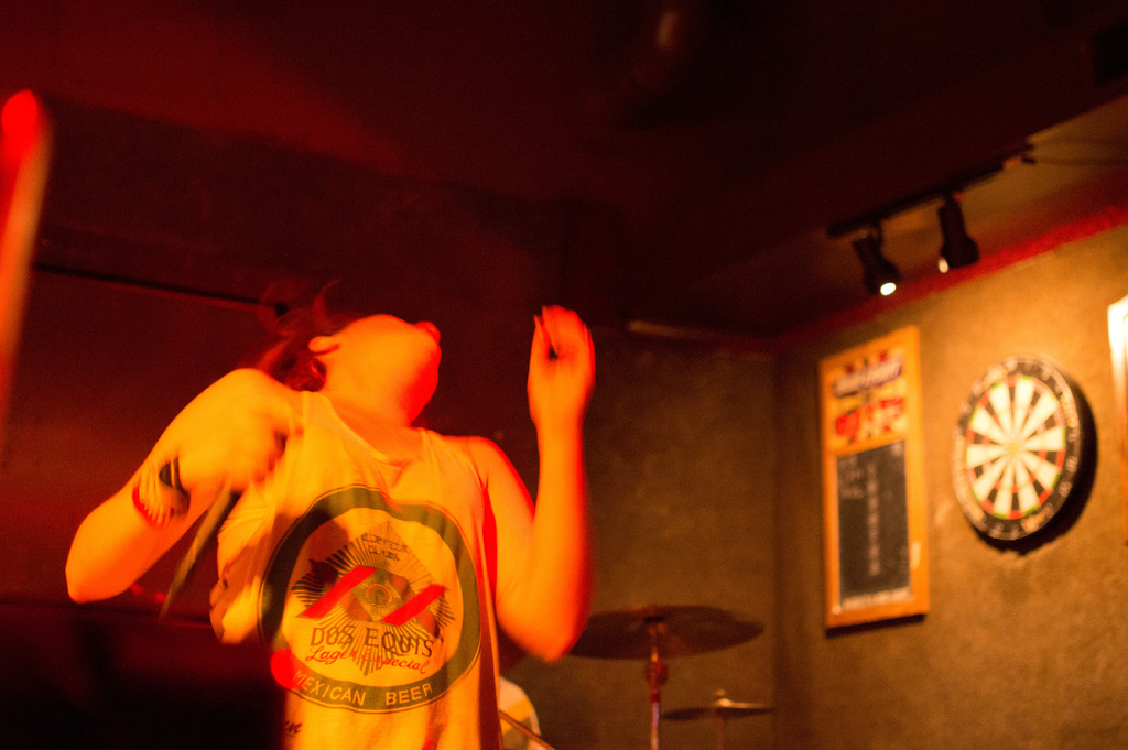 Eine Person tanzt mit einem Oberteil, auf der rechten Seite sind Lichter zu sehen.