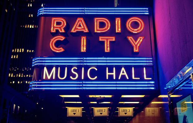 Hell erleuchtetes Radio City Music Hall in New York City mit einem "Radio City"-Schild und mehreren kleineren Schildern auf der rechten Seite.