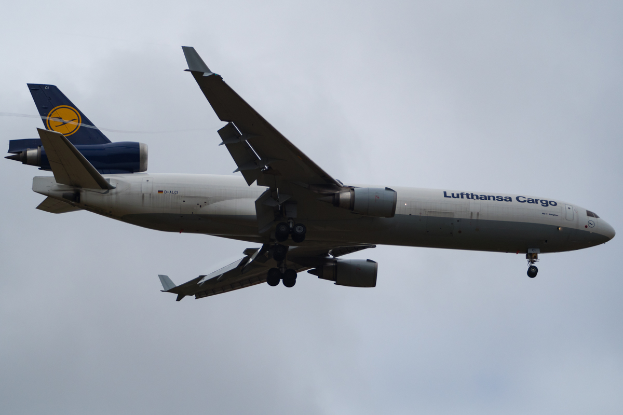 Ein Lufthansa Cargo Boeing 777-300ER-Flugzeug im Flug, mit sichtbarem Text an der Seite, das durch einen Himmel voller weißer, flauschiger Wolken fliegt.