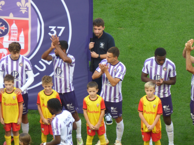 Eine Gruppe junger Jungs auf einem Fußballfeld, die klatschen, mit einem Banner und Logos im Hintergrund.