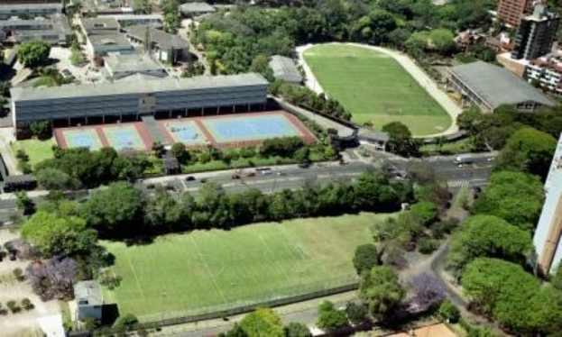 Luftaufnahme eines Fußballfelds auf dem Campus der University of Sydney, umgeben von Bäumen, Gebäuden und Fahrzeugen, die die Stelle eines neuen Sportkomplexes markieren.