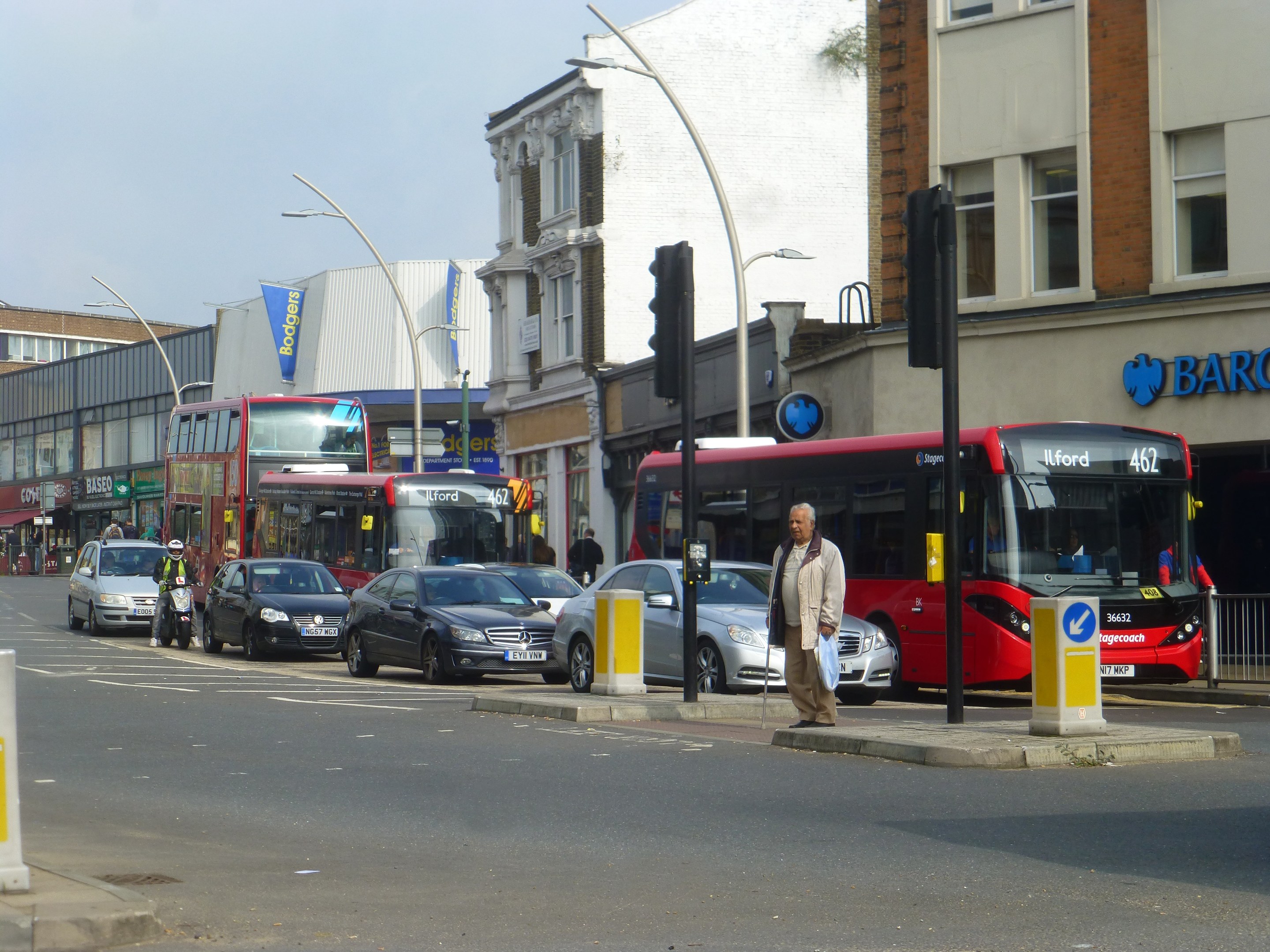 Ein roter Doppeldeckerbus fährt auf einer von hohen Gebäuden gesäumten Stadtstraße, umgeben von Fußgängern, Radfahrern und Ampeln.