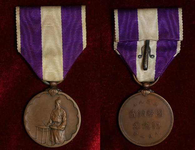 Zwei Medaillen mit lila und weißen Bändern, beschriftet mit Text, auf einer maronenfarbenen Oberfläche.