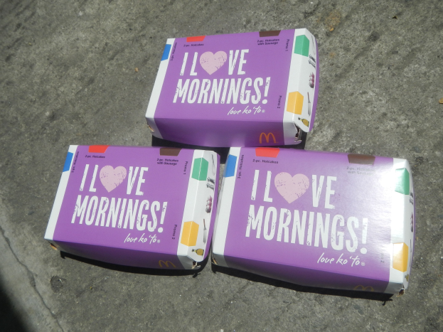 Drei buntfarbene McDonald's 'I Love Mornings'-Schachteln mit dem McDonald's-Logo und weißer, fetter Schrift auf einem hellblauen Himmel.