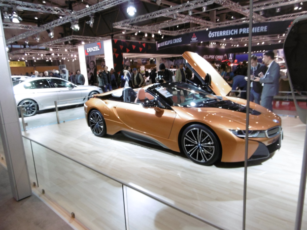 Schwarzer BMW i8 Roadster mit glänzender Lackierung und Chromakzenten, präsentiert auf der IAA in Frankfurt, umgeben von formell gekleideten Gästen in einer Atmosphäre der Aufregung.