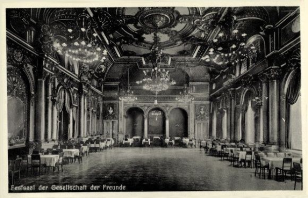 Schwarzes und weißes Foto eines großen Raumes mit Tischen, Stühlen, Säulen, Bögen und Kronleuchtern, beschriftet mit "Festival der Gesellschaft der Freunde, Berlin" unten.