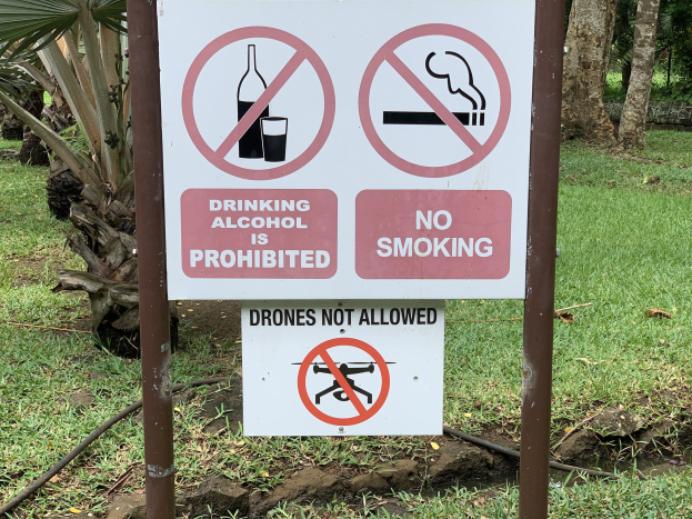 Verbotstafel für Alkoholkonsum und Rauchen mit Bäumen und Gras im Hintergrund.