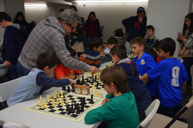 Kinder beim Schachspielen mit Erwachsenen im Hintergrund
