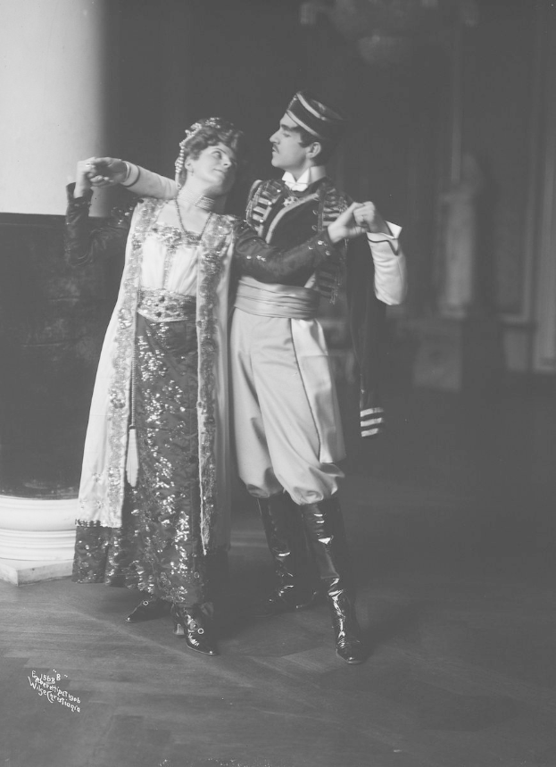 Schwarz-weißes Foto eines Mannes und einer Frau, die in einem Ballsaal tanzen, mit einer Säule und einer Wand im Hintergrund; der Mann trägt Schuhe, was auf eine Vorstellung hinweist.