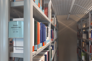 Eine Bibliothek mit Bücherregalen voller Bücher, Deckenleuchten und einer Wand im Hintergrund.