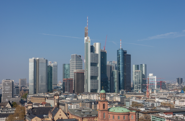 Die Skyline von Frankfurt aus der Vogelperspektive, mit einem prominenten Wolkenkratzer in der Mitte und anderen Gebäuden und Bäumen im Hintergrund.