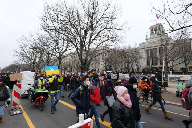 Eine große Gruppe von Menschen marschiert auf einer Demonstration in Washington, D.C. am 21. Januar 2020 mit Schildern, Fahrrädern, Bäumen und einem Gebäude im Hintergrund bei klarem blauem Himmel.
