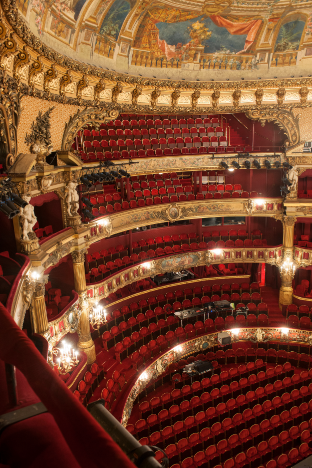 Ein Blick hinter die Kulissen der Opernhaus-Bühne im Londoner Royal Opera House, mit Sitzreihen, Geländern, Säulen, Deckenleuchten, Wandskulpturen und einer Deckenmalerei.