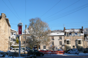 Fahrzeuge auf einer schneebedeckten Straße mit Häusern, Bäumen und Strommasten im Hintergrund, alles mit Schnee bedeckt.