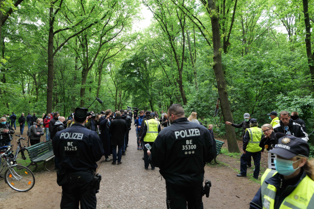 Polizisten vor einer Menschenmenge bei einer Anti-Terror-Demonstration in Berlin, mit Fahrrädern und einer Bank im Vordergrund.
