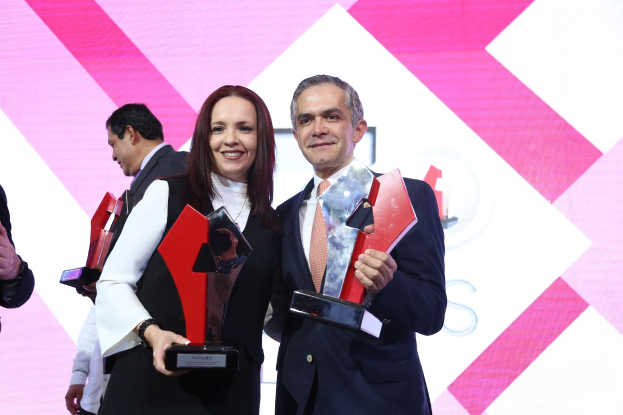 Zwei Personen auf einer Bühne mit Trophäen, die lächeln, vor einem Awards-Ceremony-Bildschirm