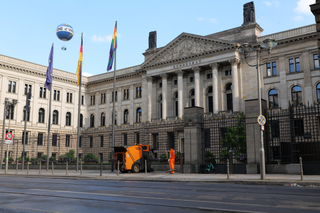 Das Bundestagsgebäude in Berlin, Deutschland, mit Flaggen, Straßenelementen und Passanten vor einem bewölkten Himmel.