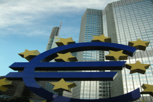 Das Euro-Zeichen steht vor dem Hauptsitz der Europäischen Zentralbank, einem modernen Gebäude, das von Bäumen umgeben ist und unter einem bewölkten Himmel in Frankfurt, Deutschland, steht.