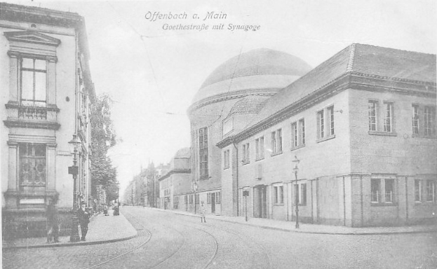 Schwarzes und weißes Foto von Offenbach am Main's Goethestraße mit einer Synagoge, Gebäuden, Straßenlaternen, Lichtern, Bäumen und Passanten.